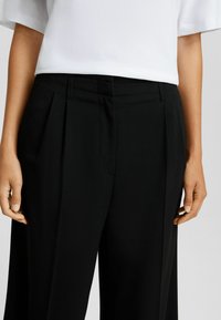 Svarta plisserade byxor med skräddarsydd passform, utrustade med sidofickor och en mjuk tygtextur, kombinerat med en vit kortärmad topp.