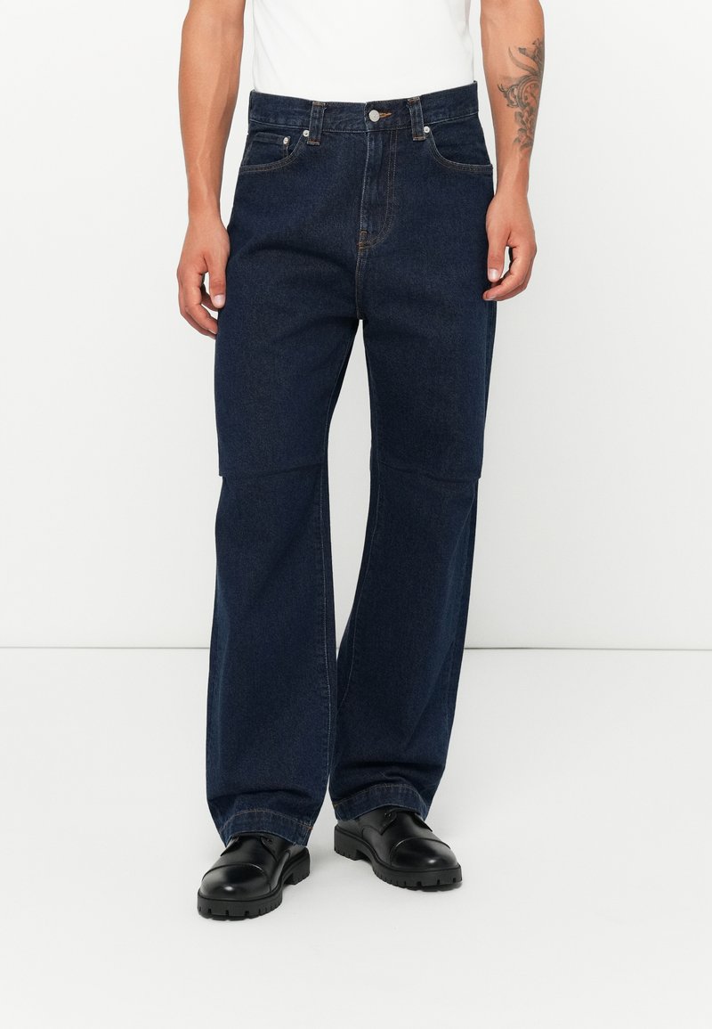 Mørkeblå denimjeans med avslappet passform, høy midje, fem lommer og subtile sømdetaljer. Kombinert med svarte sko.