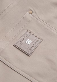 Gros plan d'une poche en tissu beige avec un patch en caoutchouc carré comportant un carré blanc centré et un texte embossé sur la surface de la poche.