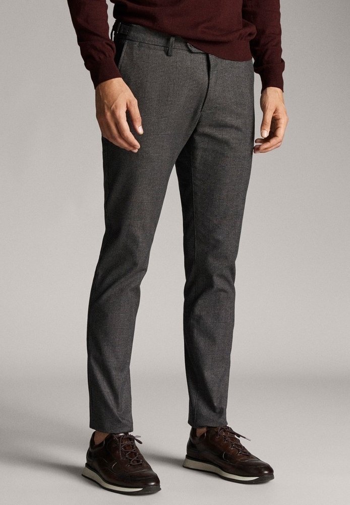 Homme portant un pantalon slim gris à carreaux avec un pull bordeaux et des baskets en cuir marron foncé, debout devant un fond uni.