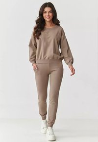 Brązowy bawełniany sweatshirt z okrągłym dekoltem i elastycznymi mankietami, w połączeniu ze spasowanymi spodniami i białymi trampkami. Gładka struktura.