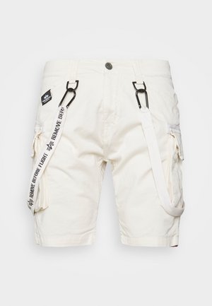 Shorts cargo en tissu de coton crème avec plusieurs poches, quincaillerie noire et une sangle amovible étiquetée "ENLEVEZ AVANT LE COMBAT."