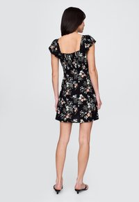 Čierne kvetinové šaty s priliehavým živôtikom, rozšírenou sukňou a volánikovými rukávmi. Materiál má viacfarebné kvetinové vzory.