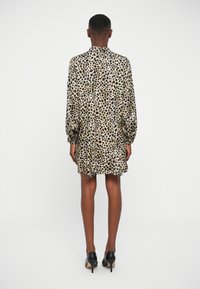 Vestido de estampado de leopardo con mangas largas, tela suave, espalda con pliegues y forma relajada. Combinado con zapatos de tacón negros.