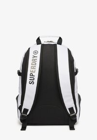 Sac à dos noir et blanc avec des bretelles réglables, une fermeture éclair et un logo "SUPERDRY" bien en vue à l'avant. Extérieur en texture lisse.