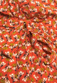 Czerwony materiał z kwiatowym wzorem, z białymi kwiatami i zielonymi liśćmi. Zawiera zawiązany detal dla dodatkowego efektu. Teksturowana powierzchnia.