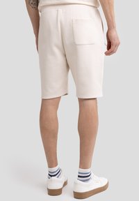 Beige bomulds shorts med en baglomme, ribbet tekstur og elastisk talje, parret med hvide sneakers og stribede sokker.