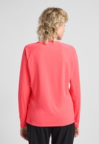 Maglietta sportiva a maniche lunghe di un rosa brillante, realizzata in un tessuto liscio e elasticizzato, con maniche raglan e un colletto a girocollo semplice.