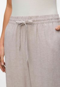 Lichtbeige broek met een trekkoord in de taille, gemaakt van zachte, gestructureerde stof. Heeft een elastische tailleband en een losse pasvorm.