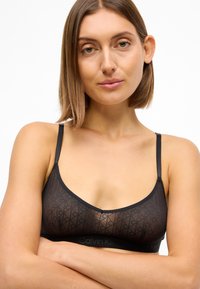 Sort bralette med et gennemsigtigt geometrisk mønster, justerbare stropper og en solid kant med "Calvin Klein" logo. Enkel og moderne design.