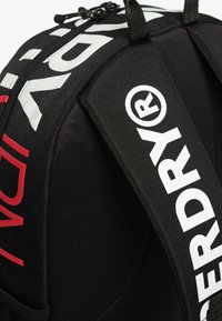 Zaino nero con spallacci imbottiti, caratterizzato da grande testo bianco "Superdry®" e una cerniera sopra.