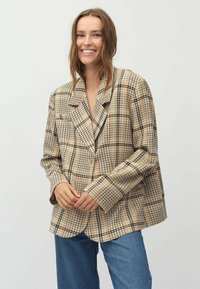 Beige kariertes Blazer mit lockerer Passform, im doppelten Knopfdesign, großen Revers und schwarzen Akzenten. Getragen mit blauen weit geschnittenen Jeans.