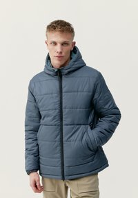 Podložena jakna temno sive barve, ki ima kapuco, sprednji zadrgo in elastične manšete. Gladka, vodoodporna tkanina z navpičnimi šivi.