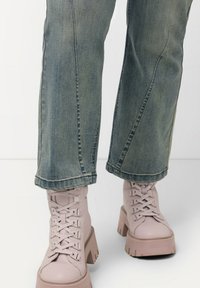 Vaaleanpunaiset nauhakenkä chunky-bootsit, joissa on paksu korko, yhdistettyinä sinisiin haalistuneisiin farkkuihin, joilla on suorainen leikkaus ja hieman risat lahkeet.