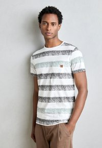 Camiseta de manga corta a rayas en blanco, negro y verde claro, con cuello redondo y un bolsillo en el pecho, hecha de algodón texturizado.