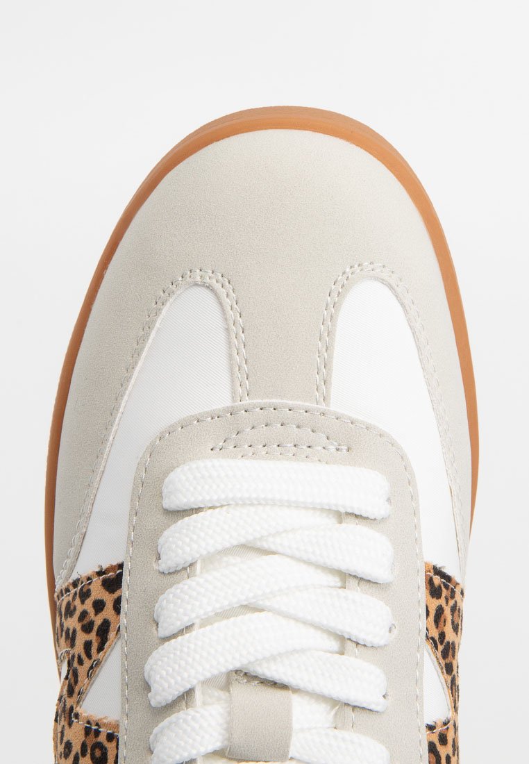 Zapatilla con diseño beige y blanco, materiales de ante y textil, con acentos de estampado de leopardo y cordones blancos. Suela de goma.