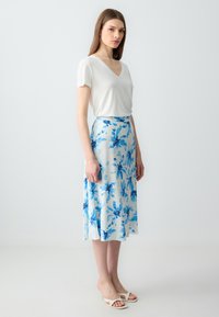 Maglietta bianca a V abbinata a una gonna fluida di colore azzurro chiaro con un motivo floreale. La gonna presenta accenti floreali blu ed è di lunghezza midi.