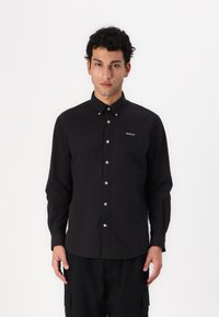 Fekete gombos ing, sima anyagból készült, klasszikus gallérral, fehér gombokkal és egy kis "Barbour" logóval a mellkasán.
