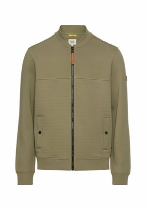 Olivengrøn jakke med bomberdesign, med lynlås foran, kontrasterende quiltet tekstur og to forlommer med sorte knapper.