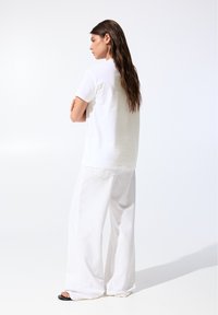 T-shirt en coton blanc à manches courtes, coupe décontractée, associé à un pantalon large blanc. Tissu texturé, design minimaliste, sans accents visibles.