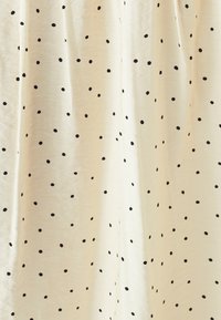 Krémová tkanina s černými puntíky, s jemnou strukturou a lehkým splývavým vzhledem. Puntíky se liší velikostí a jsou rovnoměrně rozmístěny.