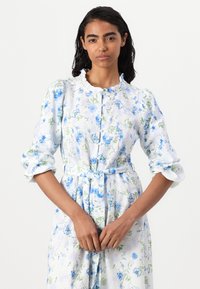 Vestido com estampa floral em tons de azul claro e verde, apresentando frente com botões, colarinho com babados e cintura com cinto, além de mangas longas e franzidas.