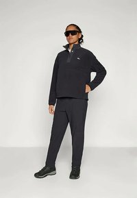 Schwarzer Fleece-Pullover mit halbem Reißverschluss und Brusttasche, kombiniert mit passenden schwarzen Hosen und schwarzen Turnschuhen, die ein simples Design aufweisen.