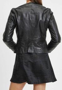 Giacca in pelle nera dal design aderente, con texture liscia e spalle strutturate, abbinata a una gonna nera con motivo fantasioso.