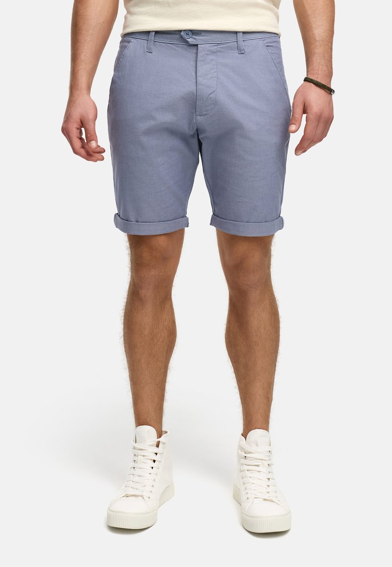 Helle blaue Baumwollshorts mit umgeschlagenen Säumen, ausgestattet mit einem Knopfverschluss und Fronttaschen, kombiniert mit weißen High-Top-Sneakern.