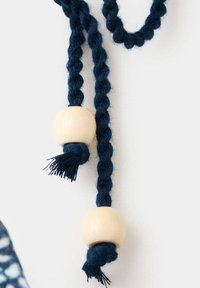 Deux cordons torsadés bleu foncé, chacun agrémenté d'une grosse perle ronde en bois clair et aux extrémités nouées sur un fond blanc.