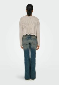 Maglione a coste di colore beige chiaro, corto, con un motivo testurizzato; abbinato a jeans azzurri a zampa d'elefante con effetto sbiadito e orlo grezzo.