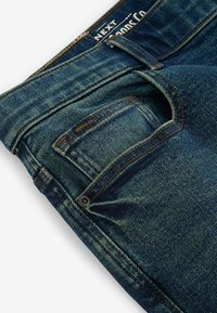 Donkerblauwe spijkerbroek van denim met een vervaagde textuur, voorzien van oranje stiksels, een klein voorvak en een merklabel op de tailleband.