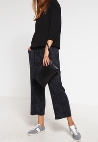 Czarna, oversize bluza, luźne ciemne spodnie w wzory, szare sneakersy z białymi detalami oraz czarna kopertówka. Casualowy strój o luźnym kroju.