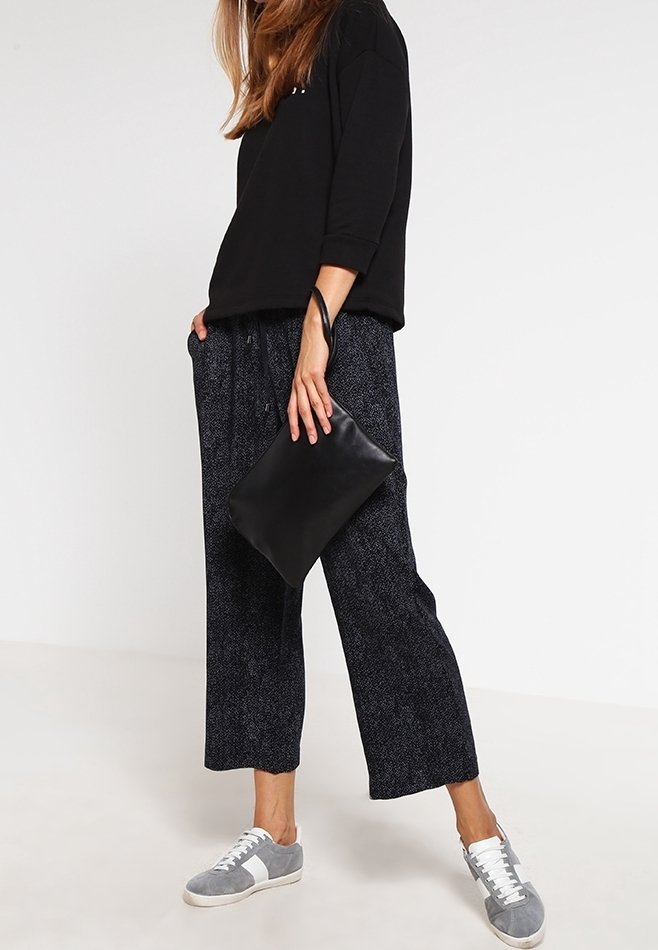 Czarna, oversize bluza, luźne ciemne spodnie w wzory, szare sneakersy z białymi detalami oraz czarna kopertówka. Casualowy strój o luźnym kroju.