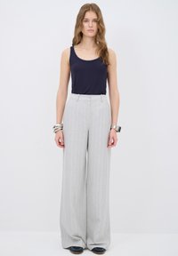 Lichtgrijze gestreepte wijde broek met een hoge taille, gecombineerd met een marineblauw tanktop. De stof lijkt glad met een subtiele glans.