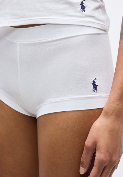 Κοντινό πλάνο ατόμου που φοράει λευκά εφαρμοστά σορτς με λογότυπο navy polo player και ορατό το τελείωμα λευκού πουκάμισου που ταιριάζει.