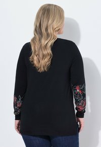 Czarna koszula z długim rękawem z kolorowym, kwiatowym haftem na rękawach. Miękka tkanina o luźnym kroju z bocznymi rozcięciami dla wygody.