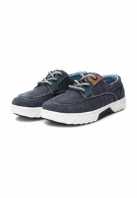 Zapatillas de lona azul marino con suela de goma blanca, cordones grises y un parche de acento marrón. Presentan una puntera redondeada y costuras en contraste.