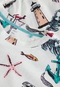 Bílé tričko z látky s barevnými námořnickými motivy, včetně majáku, ryb, vln a mořské hvězdice, s kulatým výstřihem.