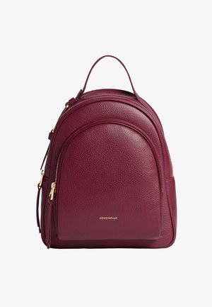 Mochila de cuero burdeos con forma redondeada, superficie texturizada y cremalleras en tono dorado. Incluye un asa superior y un bolsillo con cremallera en el lateral.