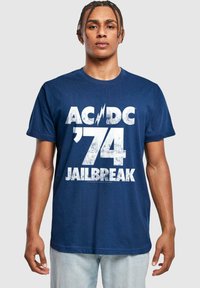 Tumedast sinise puuvillase T-särgi eesmine osa on kaunistatud valge graafilise trükiga "AC/DC '74 JAILBREAK", millel on julge, kulunud kirjastiil.