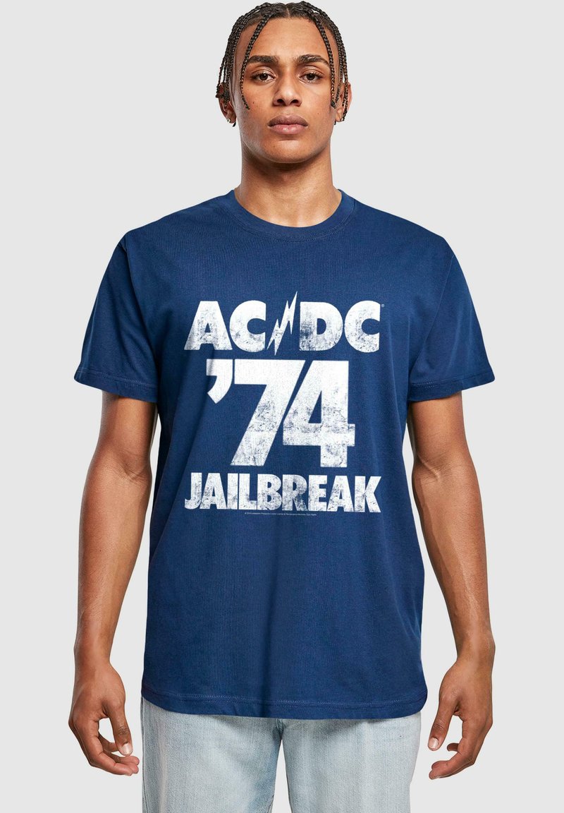 Tumedast sinise puuvillase T-särgi eesmine osa on kaunistatud valge graafilise trükiga "AC/DC '74 JAILBREAK", millel on julge, kulunud kirjastiil.
