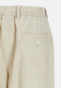 Beige Leinenhose mit elastischem Bund und Gesäßtasche, die mit einem weißen Knopf gesichert ist, zeigt die Stoffstruktur und Nähte im Detail.