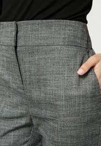 Šedé kalhoty s vzorem, s plochým předním dílem, bočními kapsami a hladkou texturou. Pás je mírně zvýšený pro přiléhavější vzhled.