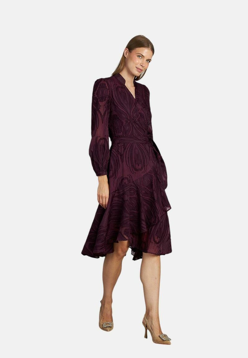 Rochie burgundă cu mâneci bufante, decolteu în V, tiv valurit și detalii florale texturate. Purtați cu tocuri bej cu embellishments.