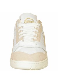 Vita läder och beige mockaskor med vita snören, platt gummisula och präglad logotyp på tungan. Har tre vita ränder på sidorna.