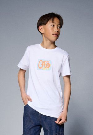 T-shirt en coton blanc avec un design graphique abstrait coloré en orange et bleu, à manches courtes et à col rond.