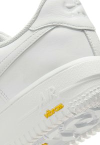 White sneaker with textured leather upper and rubber sole. Features "AIR" embossed and "vibram" logo in yellow, ensuring grip and support.
