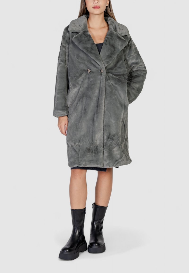 Cappotto in pelliccia sintetica grigia con ampio colletto, bottoni doppi e maniche lunghe, abbinato a stivaletti neri alla caviglia. Materiale liscio e texture.