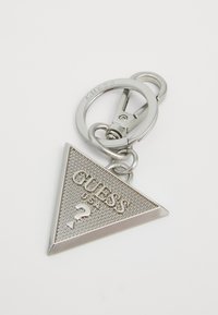 Silver triangular Guess keychain with textured surface, raised brand name "GUESS USA," and a question mark symbol attached to a key ring clasp.